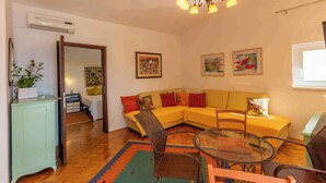 Uma sala de estar com sofá, cadeiras, mesa de vidro e obras de arte nas paredes.