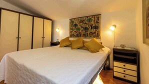 Quarto com uma cama grande, mesa de cabeceira, prateleira na parede e um adorno de parede.