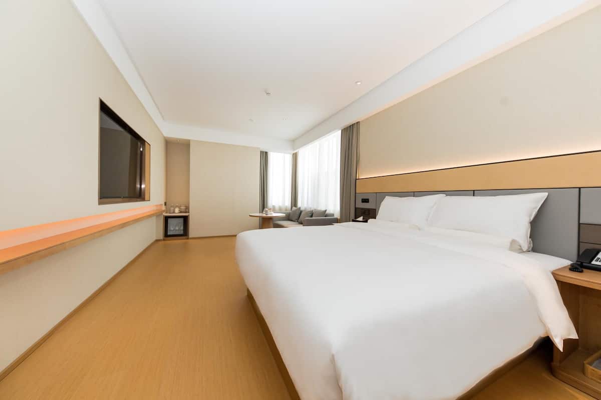 A hotel room with a large bed, a bedside table, a TV mounted on the wall, and a window with curtains.