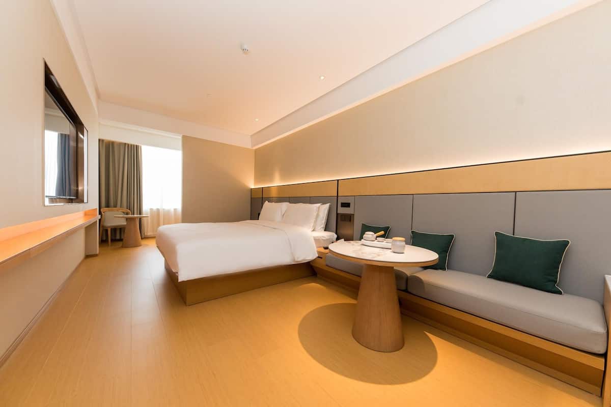 A modern hotel room with a large bed, a round table, and a sofa.