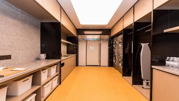 Een moderne hotelgang met een kitchenette aan de linkerkant, een wasserette aan de rechterkant, en een centrale deur naar een andere kamer.