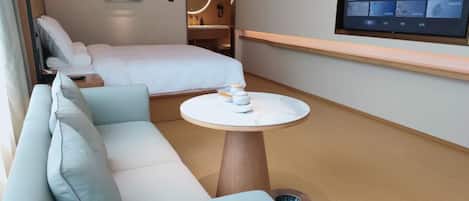 Une chambre d’hôtel moderne équipée d’un canapé, d’un lit, d’une table ronde et d’un téléviseur fixé au mur.