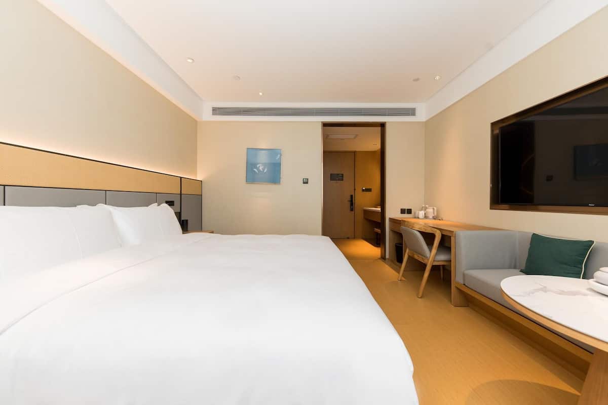 A modern hotel room with a large bed, a desk, and a seating area.
