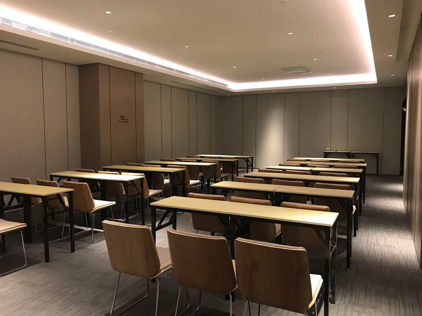 A conference room with multiple tables and chairs, equipped with ceiling lights and a carpeted floor.