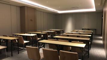 A conference room with multiple tables and chairs, equipped with ceiling lights and a carpeted floor.