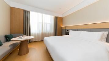 Una habitación de hotel moderna con una cama grande, una mesa redonda con una lámpara, un sofá y vistas al exterior a través de la ventana.