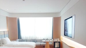 Habitación de hotel con dos camas, una mesita, televisión en la pared y ventana con cortinas.