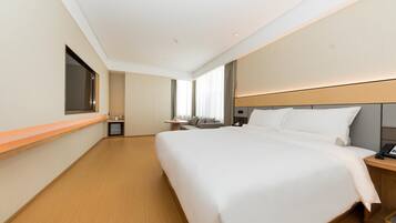 A hotel room with a large bed, a bedside table, a TV mounted on the wall, and a window with curtains.