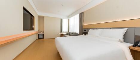 Habitación de hotel con una cama grande, una mesita de noche, un televisor montado en la pared y una ventana con cortinas.