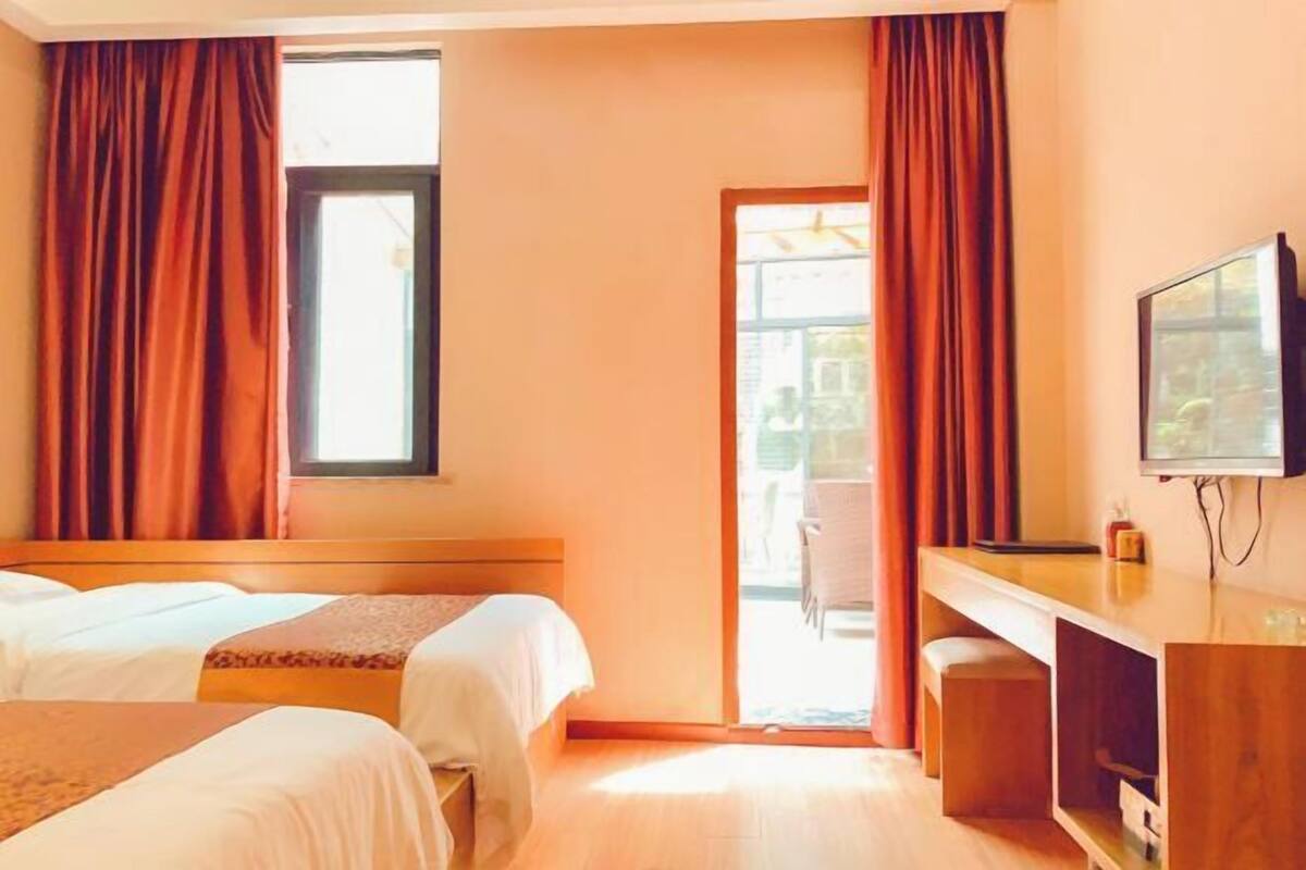 A hotel room with two beds, a desk, a television, and a window with curtains.