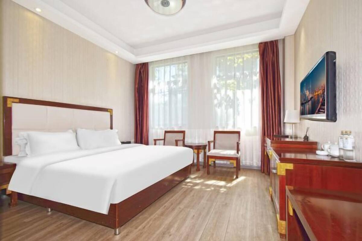 A hotel room with a large bed, a desk with a chair, a television, and a window with curtains.