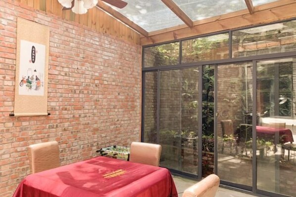A room with a brick wall, a large sliding glass door leading to an outdoor area, a table with a red tablecloth, and a ceiling fan. - Very Huating Hotel (Chongqing)