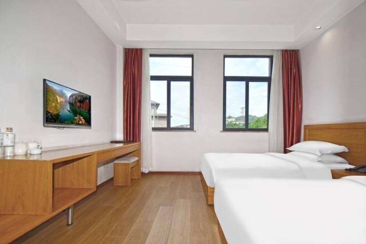 A hotel room with a bed, a desk, a TV, and a window with curtains.