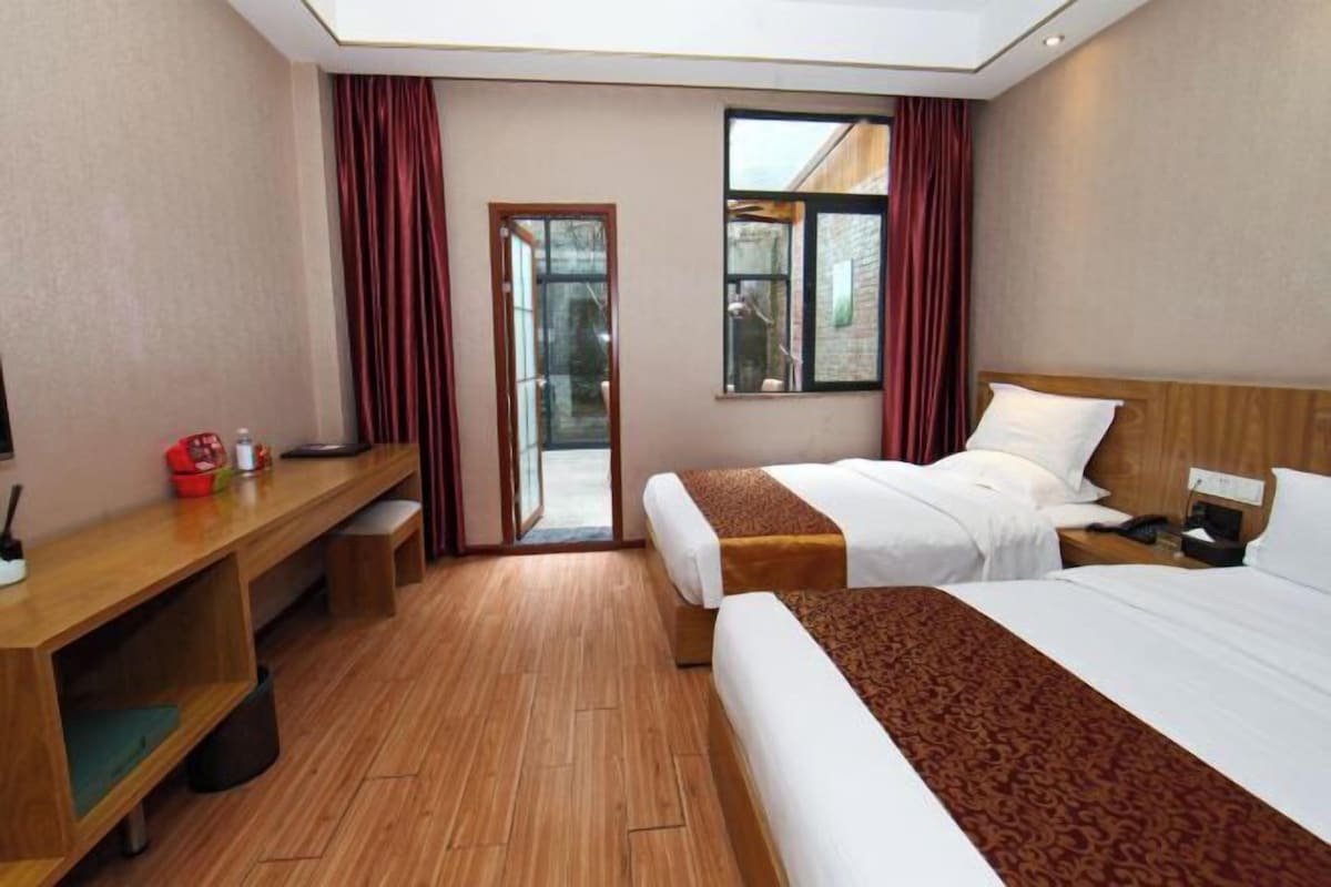 A hotel room with two beds, a desk, and a view of the outside.