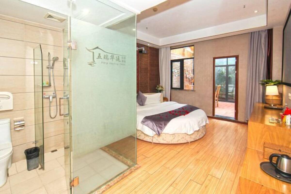 A hotel room with a glass-enclosed shower, a bed with a view, and a wooden floor.