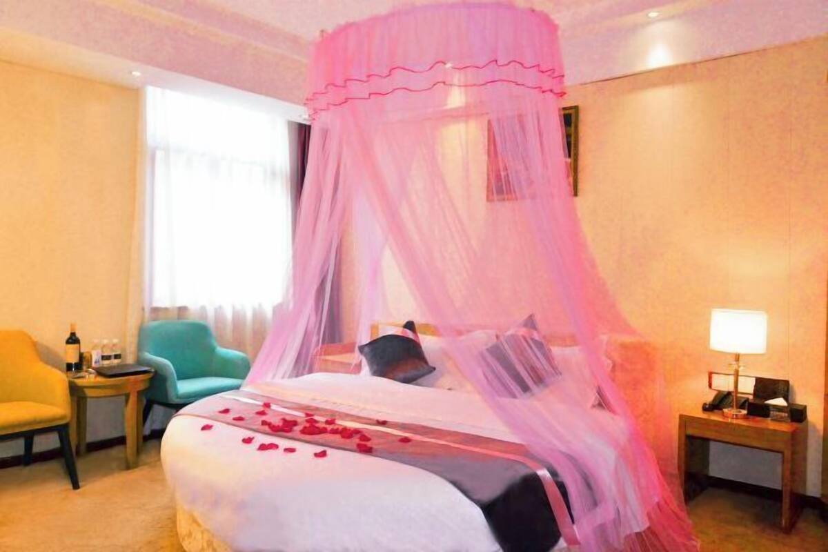 A hotel room with a bed, a nightstand, a chair, and a window with curtains.
