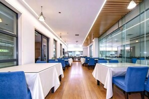 A modern dining area with tables and chairs, large windows, and a wooden floor. - Very Huating Hotel (Chongqing)