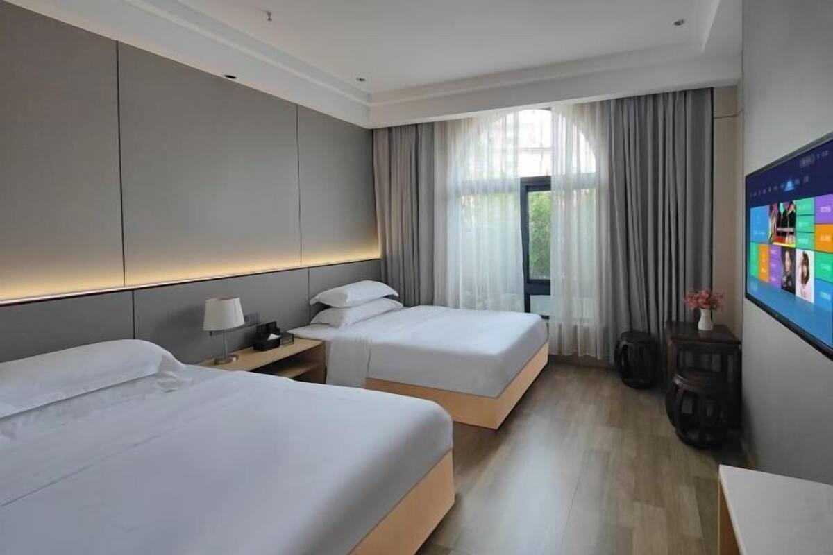 A hotel room with two beds, a TV, a desk, and a window with curtains.