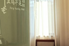 A hotel room with a window, curtains, and a wall with text indicating the hotel name. - Very Huating Hotel (Chongqing)