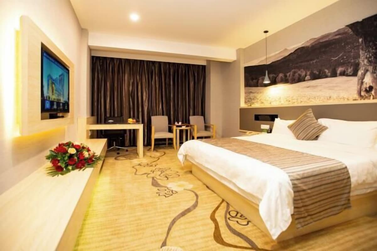 Habitación de hotel con una cama grande, un escritorio con dos sillas, un televisor y una obra de arte colgada en la pared.