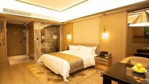Habitación de hotel con cama, mesita de noche, lámpara y una mesa de comedor con fruta.