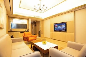 A modern living room with a flat-screen TV, a sofa, a coffee table with fruit, and a ceiling light fixture.