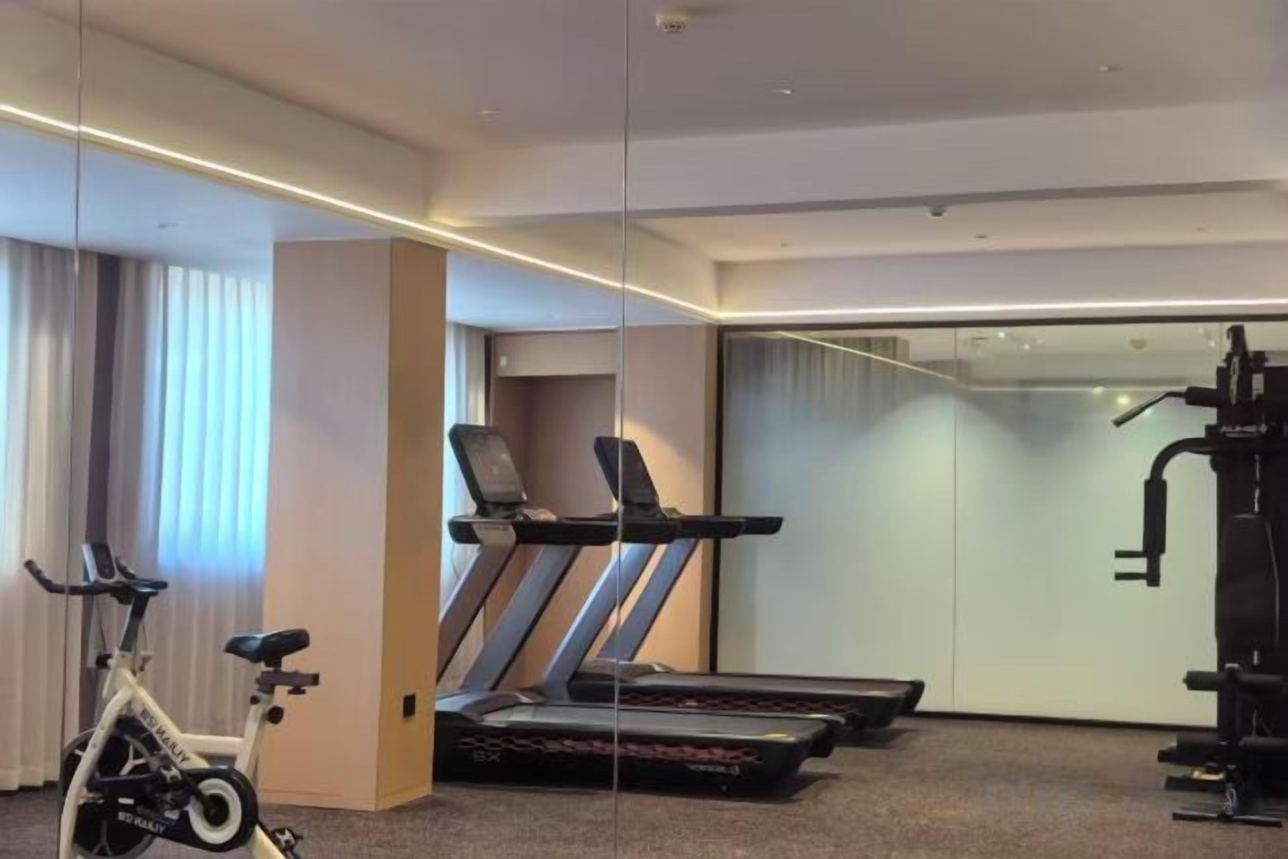 Ein Hotelzimmer mit Laufband, Heimtrainer und einem großen Spiegel.