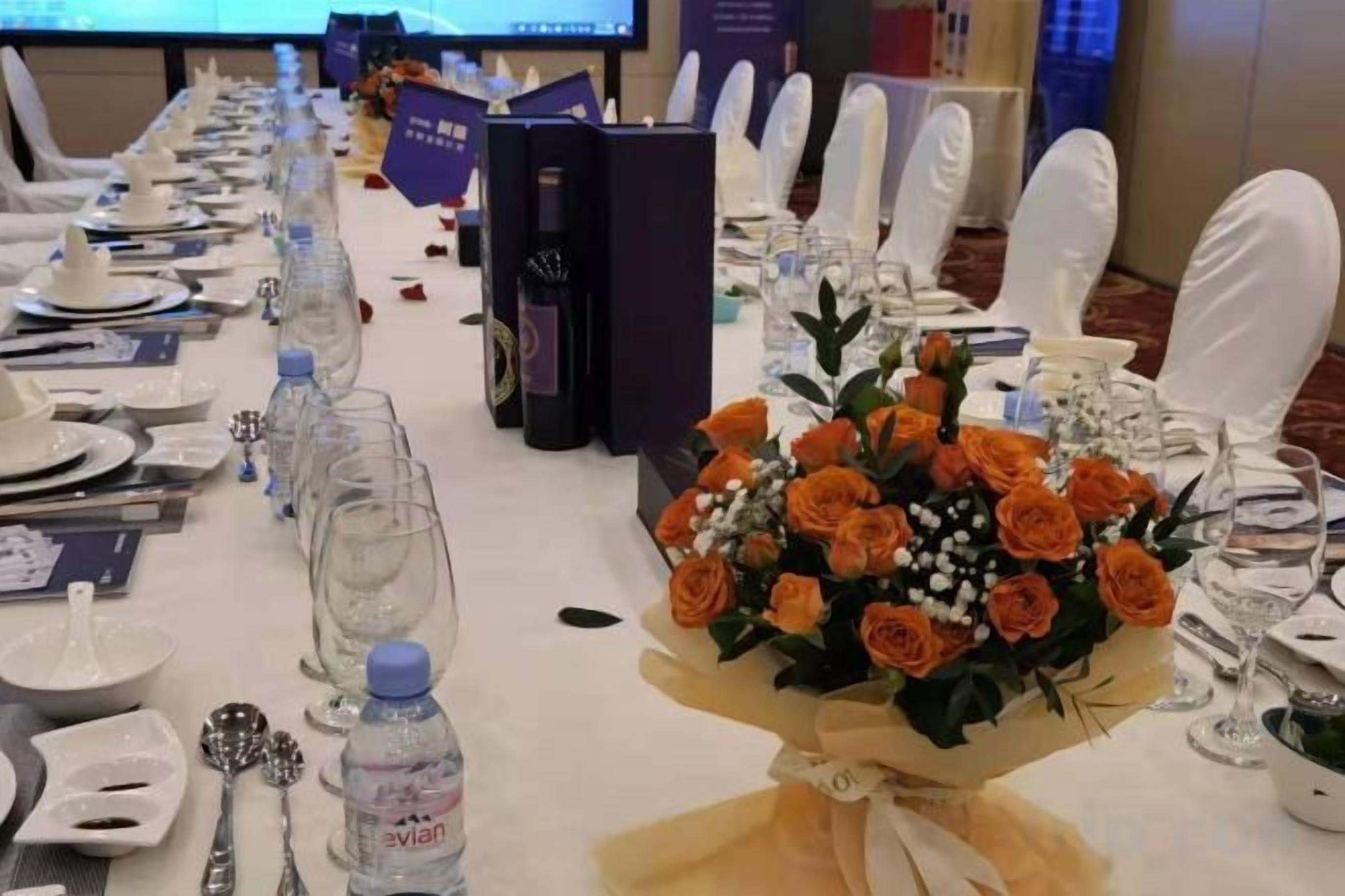 A banquet table set with plates, cutlery, water bottles, and a bouquet of flowers.
