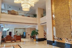 A multi-level hotel lobby with a chandelier, a large decorative wall, and a reception desk.