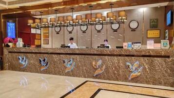 A hotel reception area with a marble counter, a digital screen, and a row of lamps.