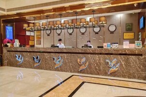A hotel reception area with a marble counter, a digital screen, and a row of lamps.
