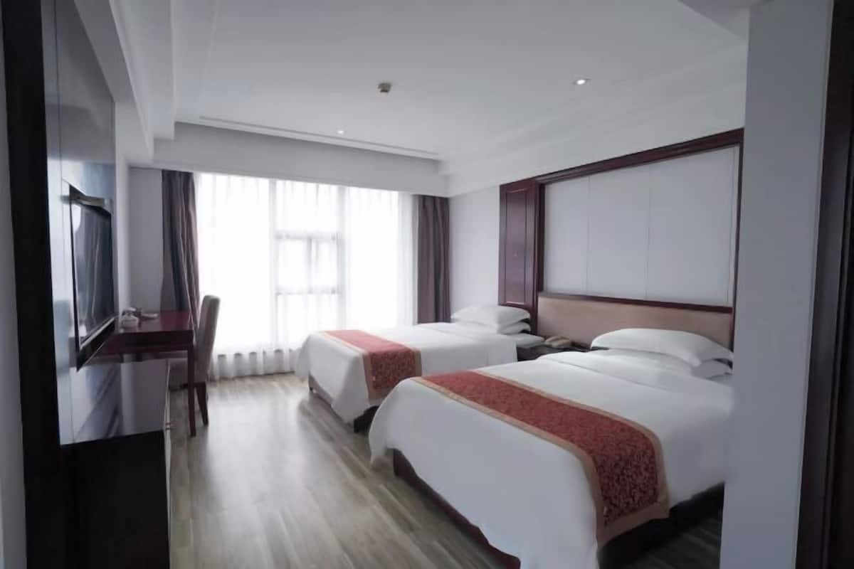 Quarto de hotel com duas camas, uma mesa, uma televisão e uma janela grande.