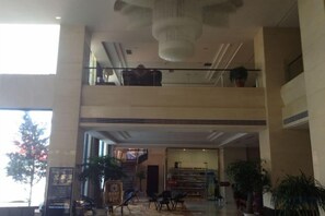 A multi-level hotel lobby with a high ceiling, a staircase, and potted plants. - Xinyuan Hotel Wanzai (Wanzai)