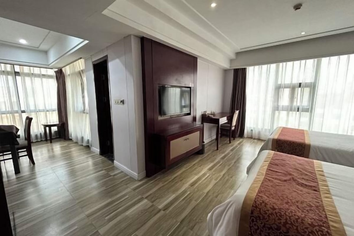 Habitación de hotel con televisión de pantalla plana, escritorio, silla y cama con colcha estampada.