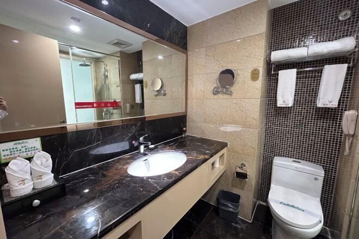 Un baño moderno con un espejo grande, un lavamanos, un inodoro y una zona de ducha.