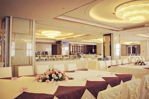 Un salón de banquetes con mesas redondas, sillas blancas y una araña.