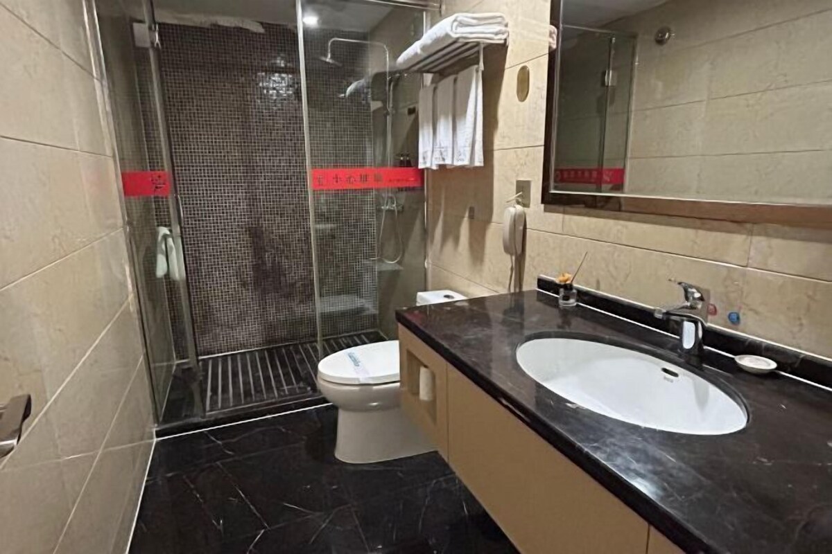 Un baño con ducha envuelta en vidrio, un inodoro y un lavamanos con un espejo arriba.