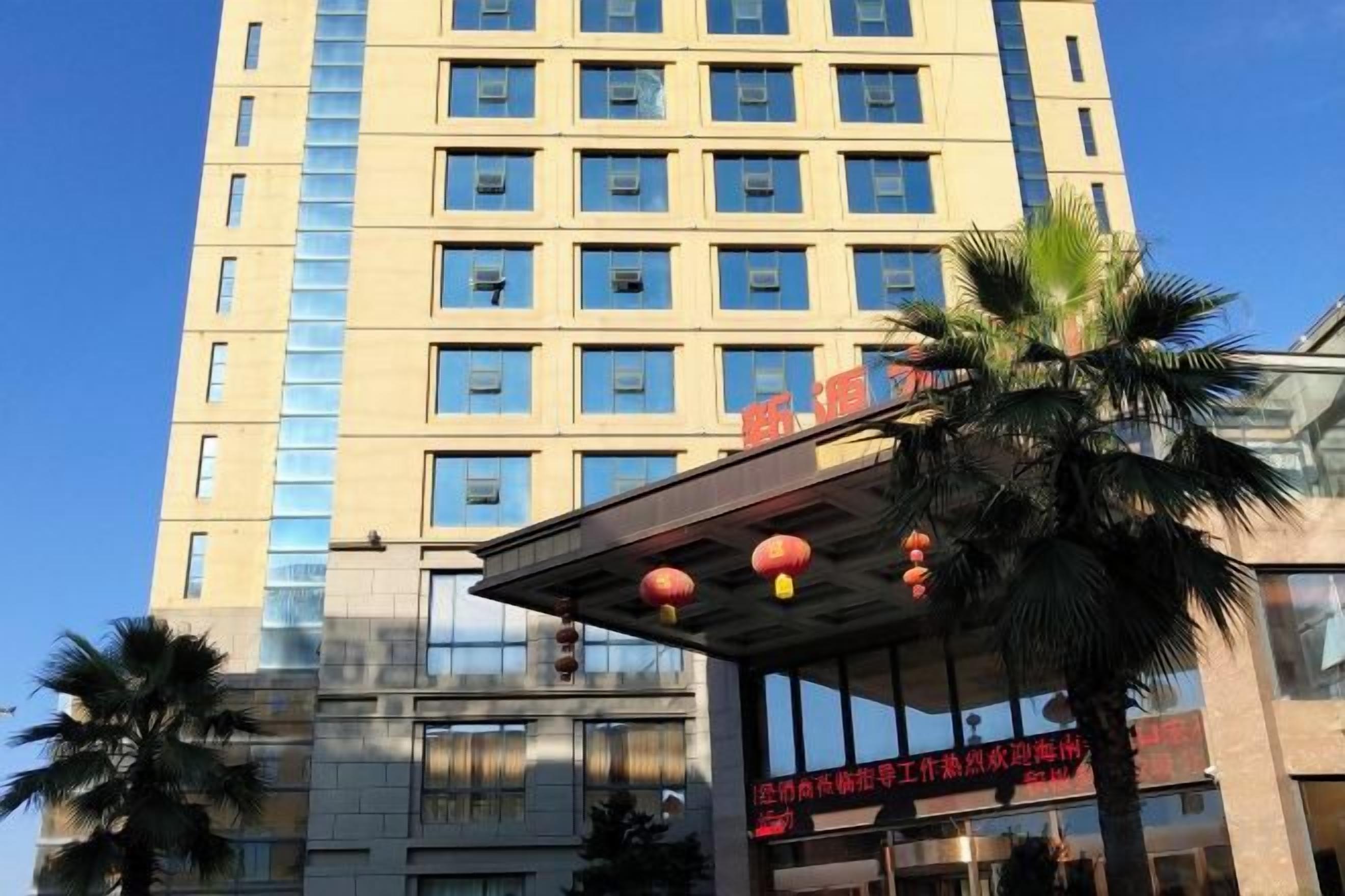 A multi-story hotel building with a modern facade, large windows, and a palm tree in the foreground.