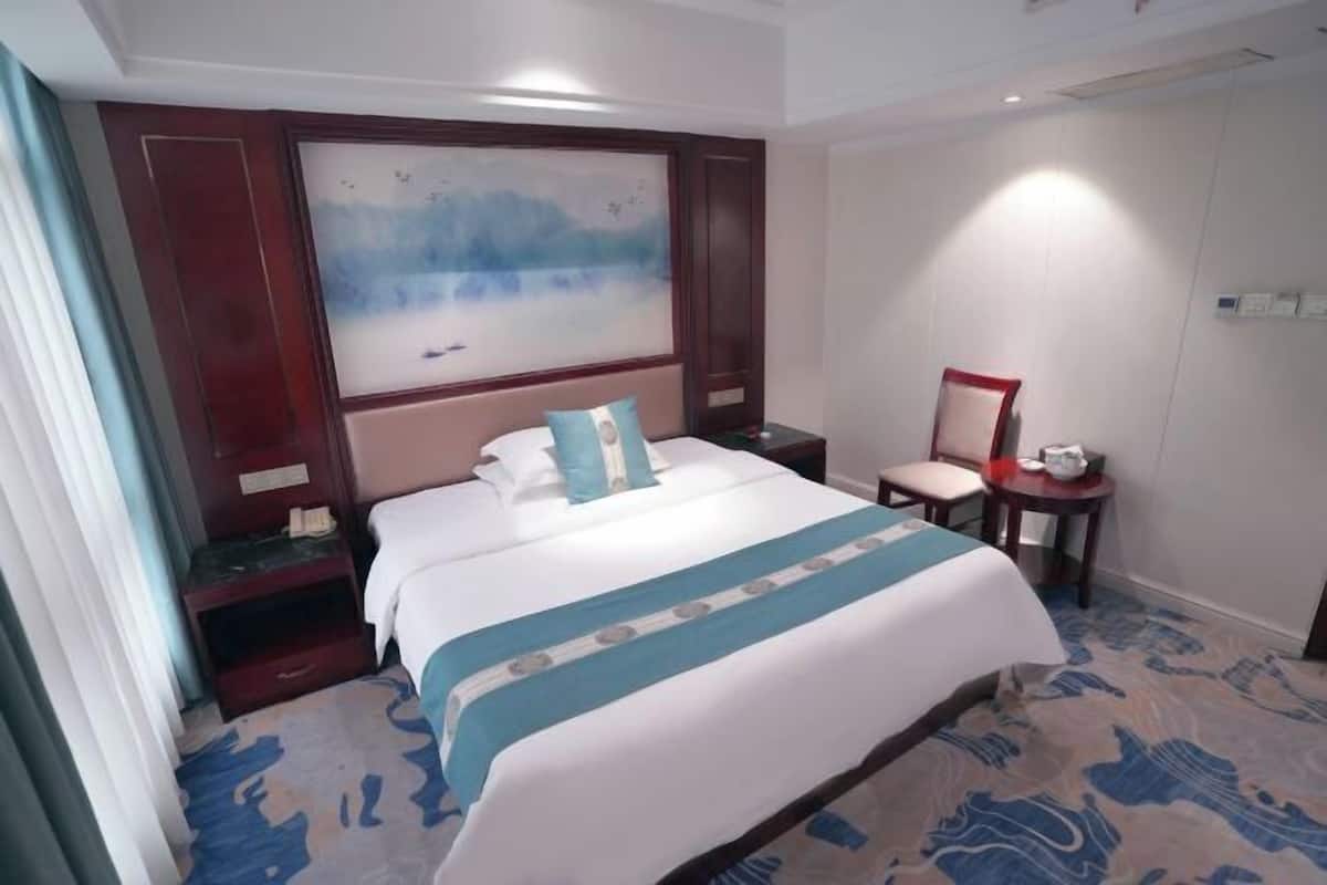Quarto de hotel com uma cama grande, uma escrivaninha, uma cadeira e um quadro na parede.
