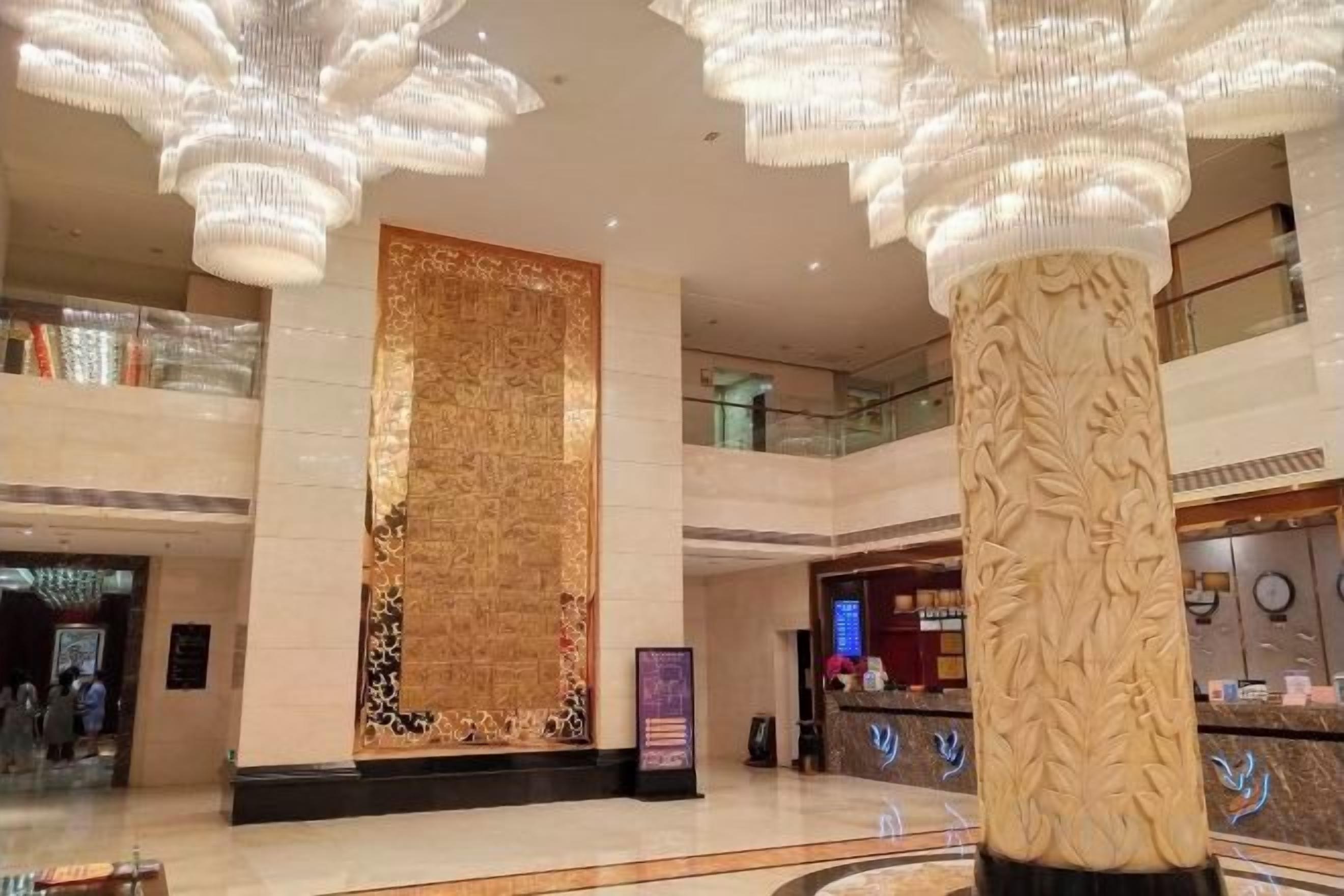 Un vestíbulo amplio con una gran pared decorativa, una mesa de recepción y un techo alto con candelabros colgantes.