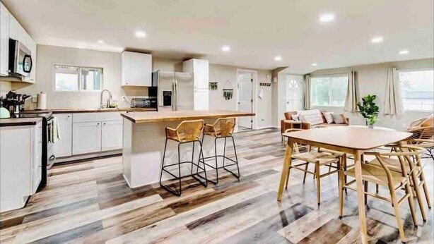 Una cocina moderna con armarios blancos, una isla central con taburetes y un comedor con mesa y sillas de madera.