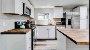 Una cocina moderna con armarios blancos, un refrigerador de acero inoxidable y una encimera de madera.