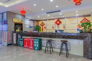 A hotel reception area with a marble counter, two stools, a plant, and red decorative elements. - Lang Ting Hotel (Shaoyang)