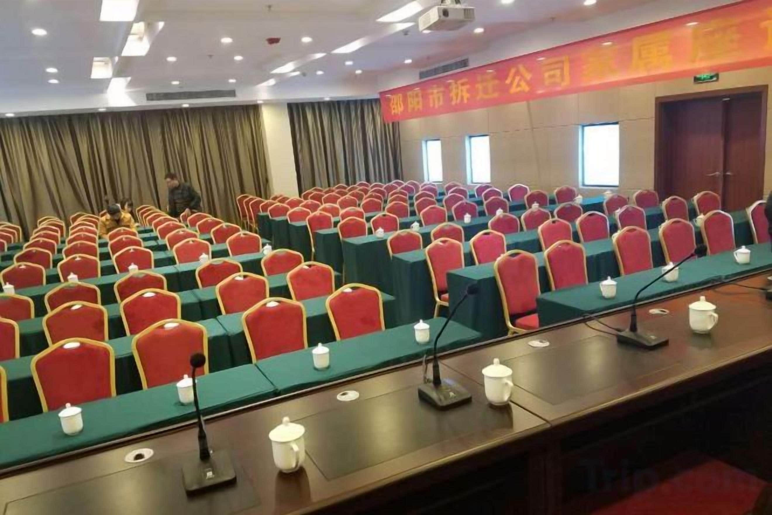 Un salón de conferencias con filas de sillas y mesas, micrófonos y un atril.