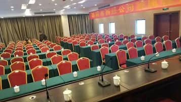 Un salón de conferencias con filas de sillas y mesas, micrófonos y un atril.