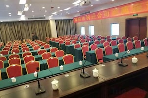 Un salón de conferencias con filas de sillas y mesas, micrófonos y un atril.