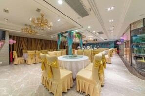 Un salón de banquetes con mesas redondas, sillas y una araña.