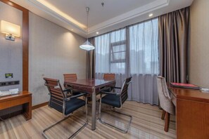 A hotel room with a wooden dining table, four chairs, a desk, a lamp, and a large window with curtains. - Lang Ting Hotel (Shaoyang)