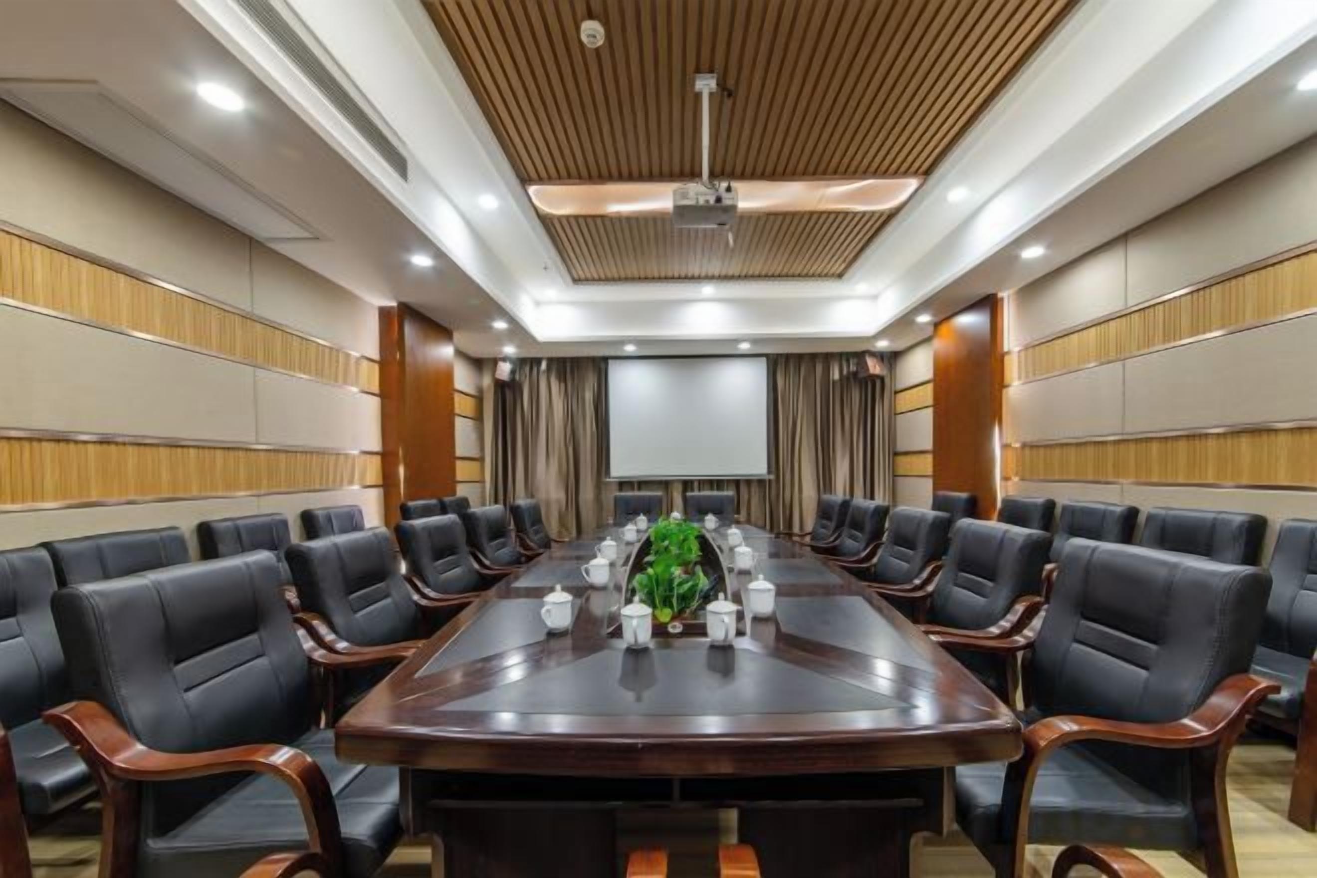 A conference room with a long table, chairs, and a projector screen.