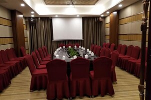 Un salón de conferencias con una mesa redonda, sillas rojas y una pantalla de proyector.